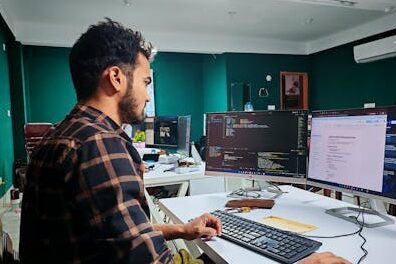 Software developer coding on dual monitors in a well-lit modern office, focused and engaged.