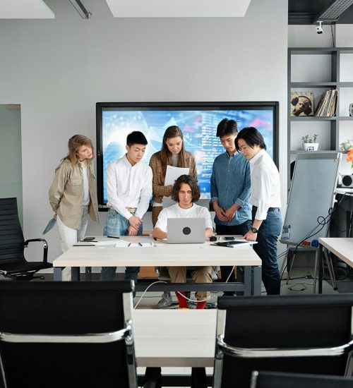 A group of colleagues collaborating around a laptop in a contemporary office environment.